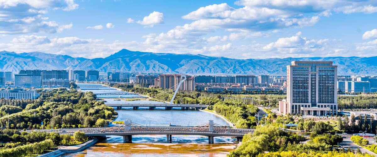 A river with a bridge, a cityscape with buildings, and mountains in the background.
