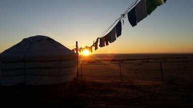 Eine Jurte mit Sonnenuntergang im Hintergrund und Gebetsfahnen.