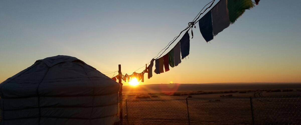 A yurt with a sunset in the background and prayer flags.