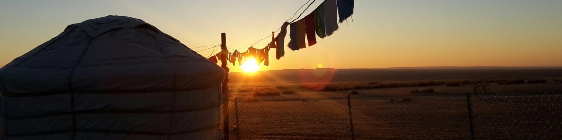 A yurt with a sunset in the background and prayer flags.
