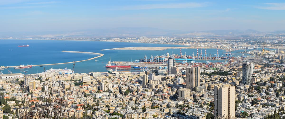 A coastal cityscape with a marina, ships, and a curved breakwater.