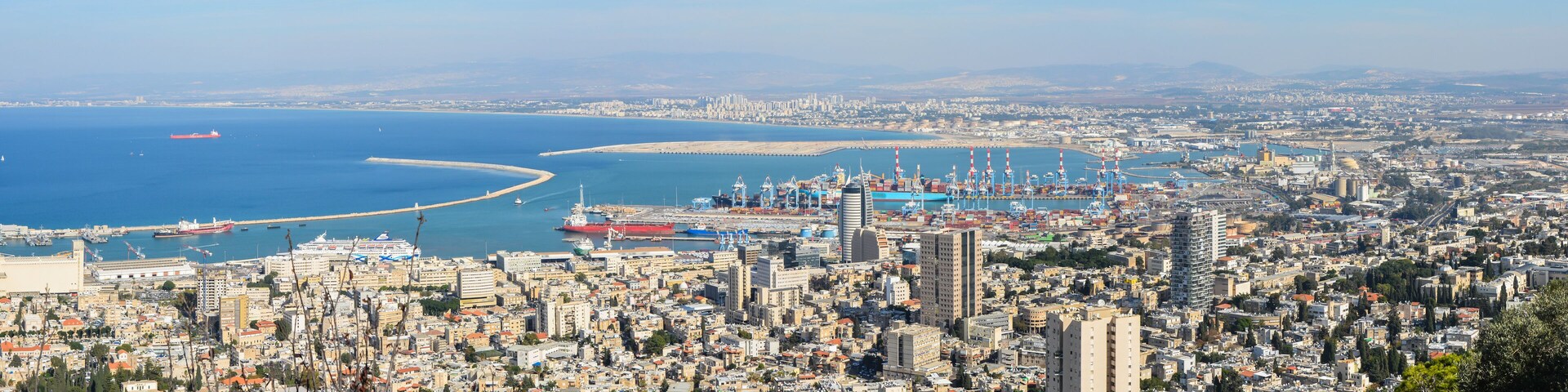 A coastal cityscape with a marina, ships, and a curved breakwater.