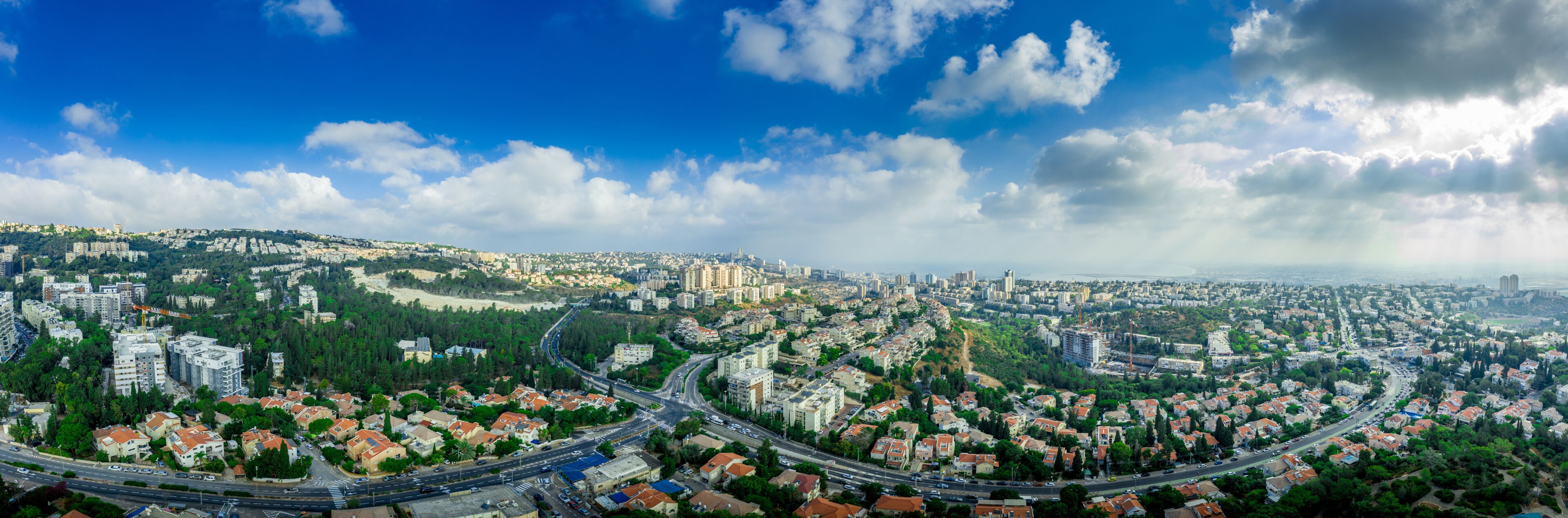 Aerial panorama of Ramot Remez and Romema modern neighborhoods with major intersecting roads modern houses with white walls and red roofs, high rising new construction in Haifa Israel with blue sky