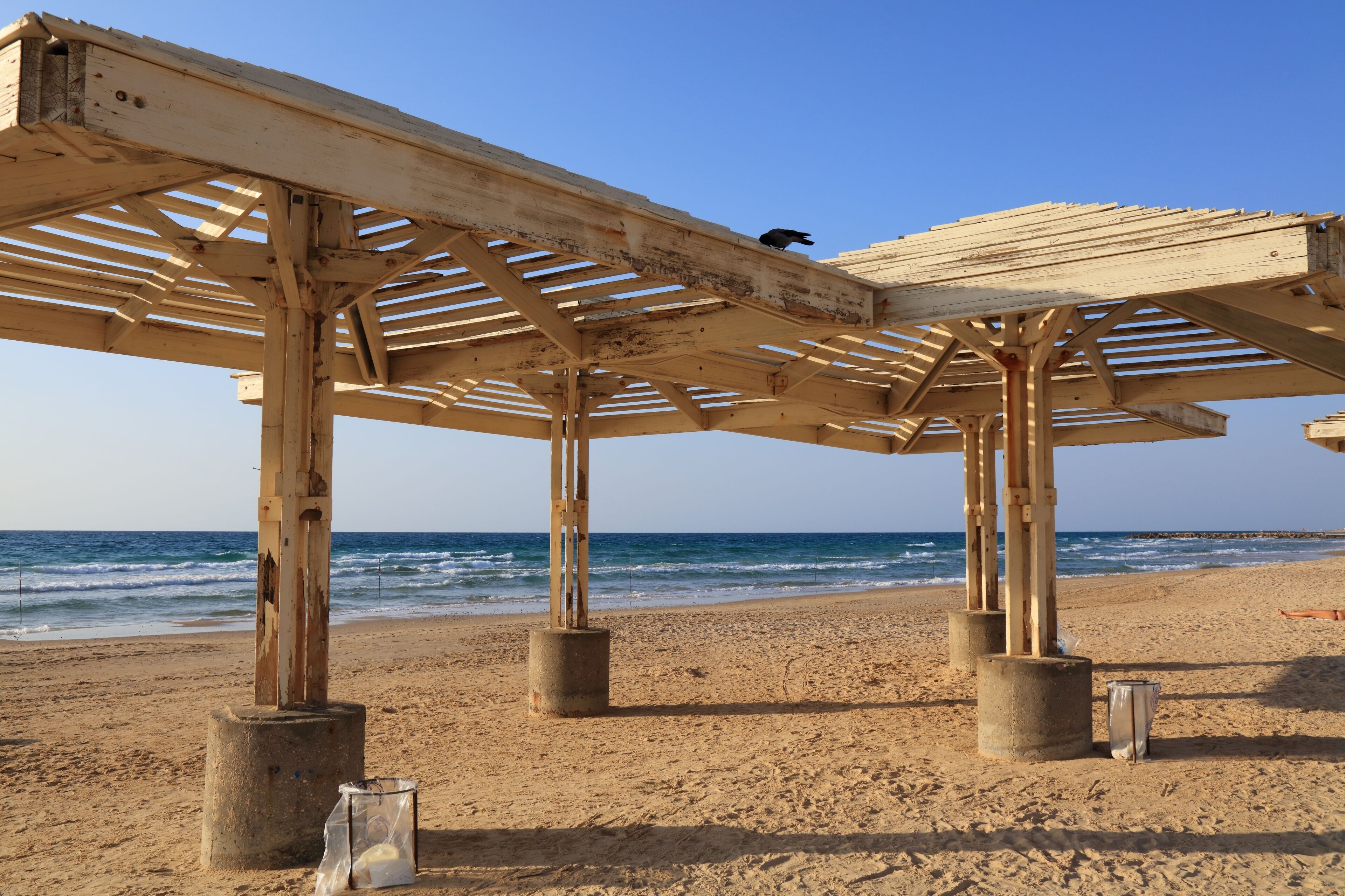 A wooden beach umbrella structure on a sandy beach with the ocean in the background.