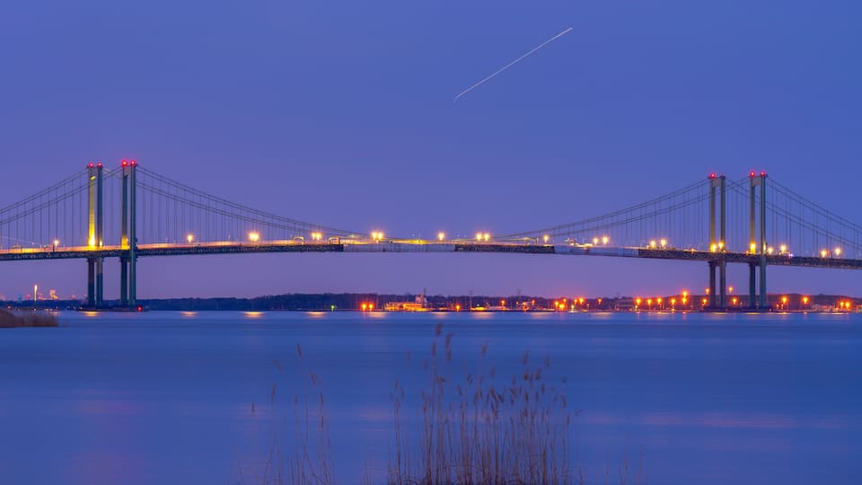A bridge spanning a body of water at dusk with lights on the structure.