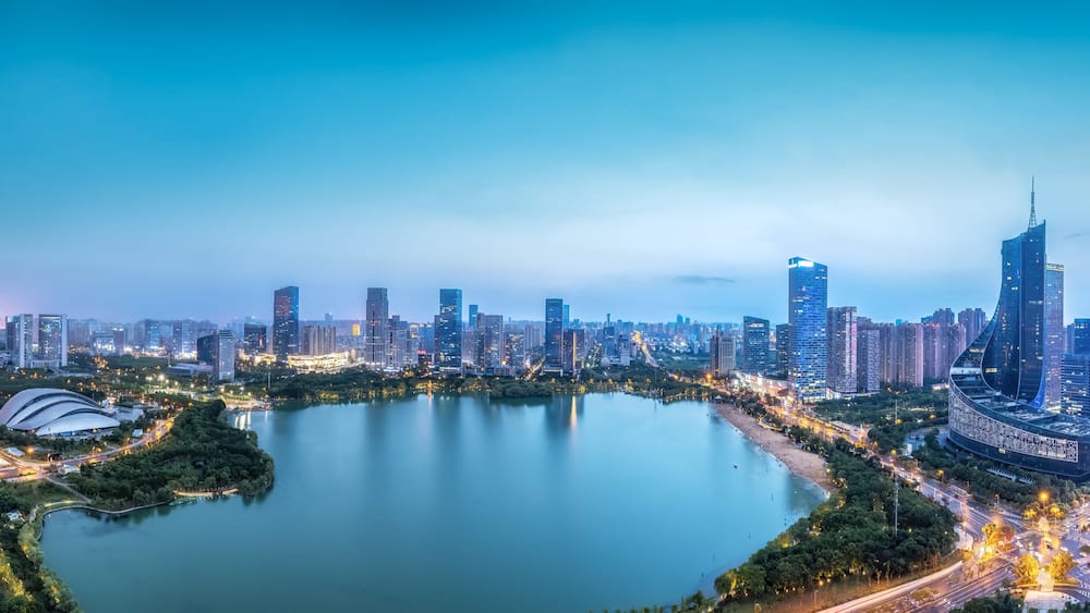 A cityscape with a large body of water, high-rise buildings, and a curved structure near the water's edge.