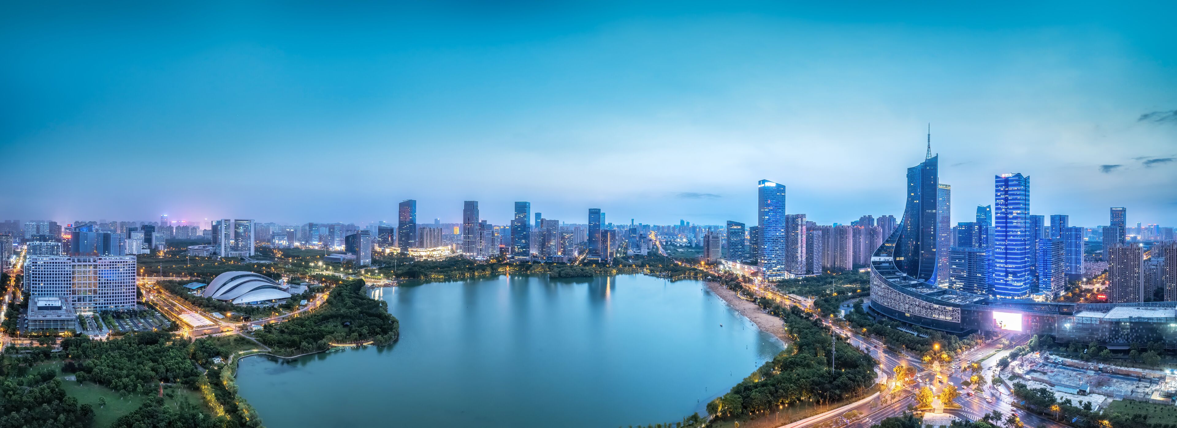 A cityscape with a large body of water, high-rise buildings, and a curved structure near the water's edge.