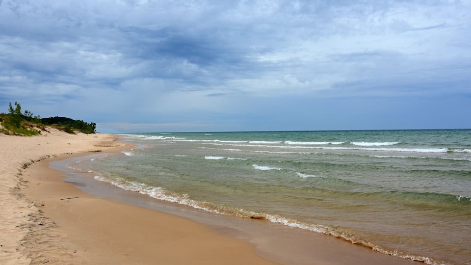 A sandy beach with gentle waves and a cloudy sky.