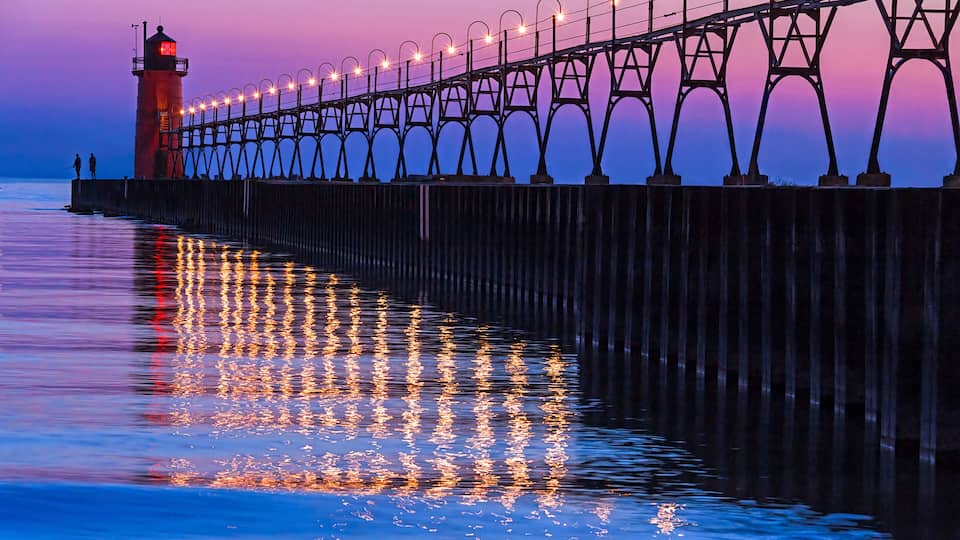 A pier with lights reflecting on the water at dusk.