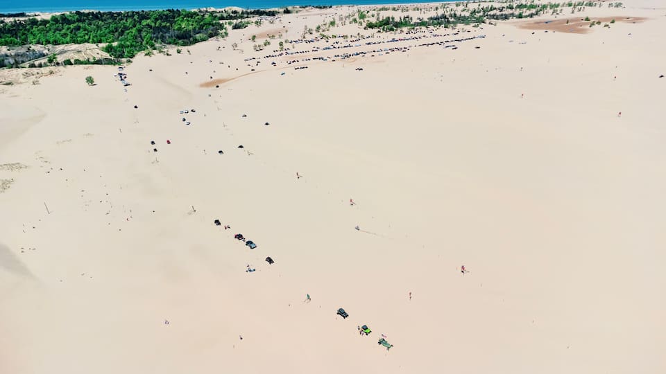 A vast sandy beach with scattered vehicles and sparse vegetation.