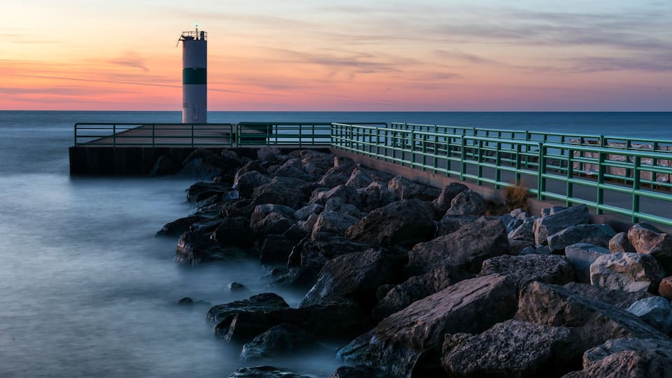 A coastal scene with a lighthouse, rocky shoreline, and a sunset.