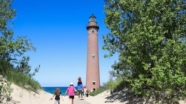 A lighthouse on a sandy path with greenery on either side and the ocean in the background.
