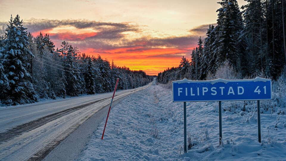 A snow-covered road with a sign for 'Filipstad 41' and a sunset in the background.