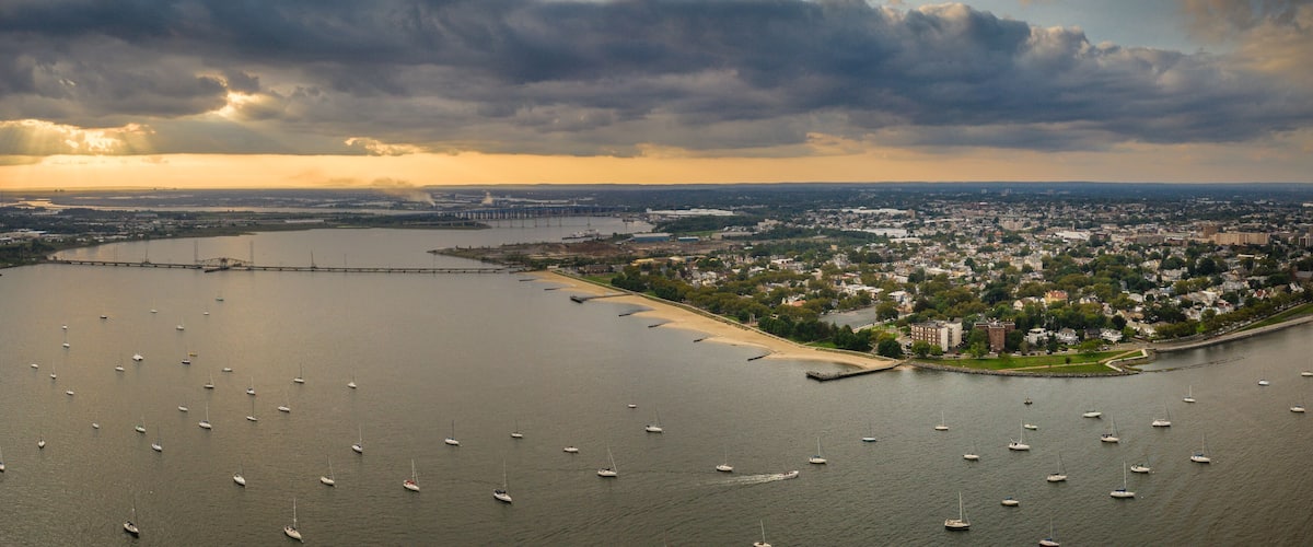 A coastal city with a large body of water, numerous sailboats, and a prominent bridge connecting two land masses.