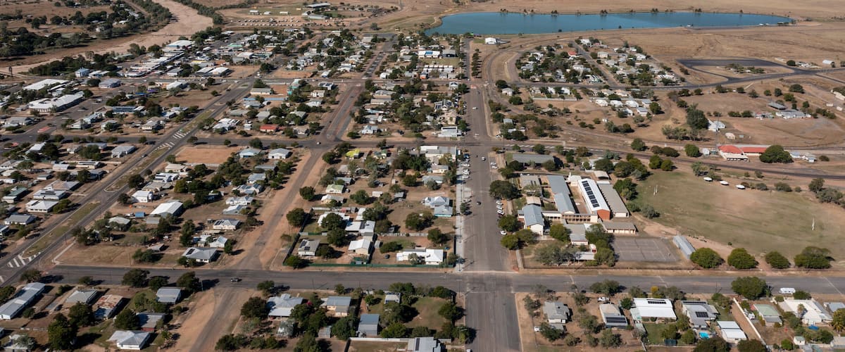 An aerial view of a town with a central road, surrounding houses, a large body of water, and open fields.