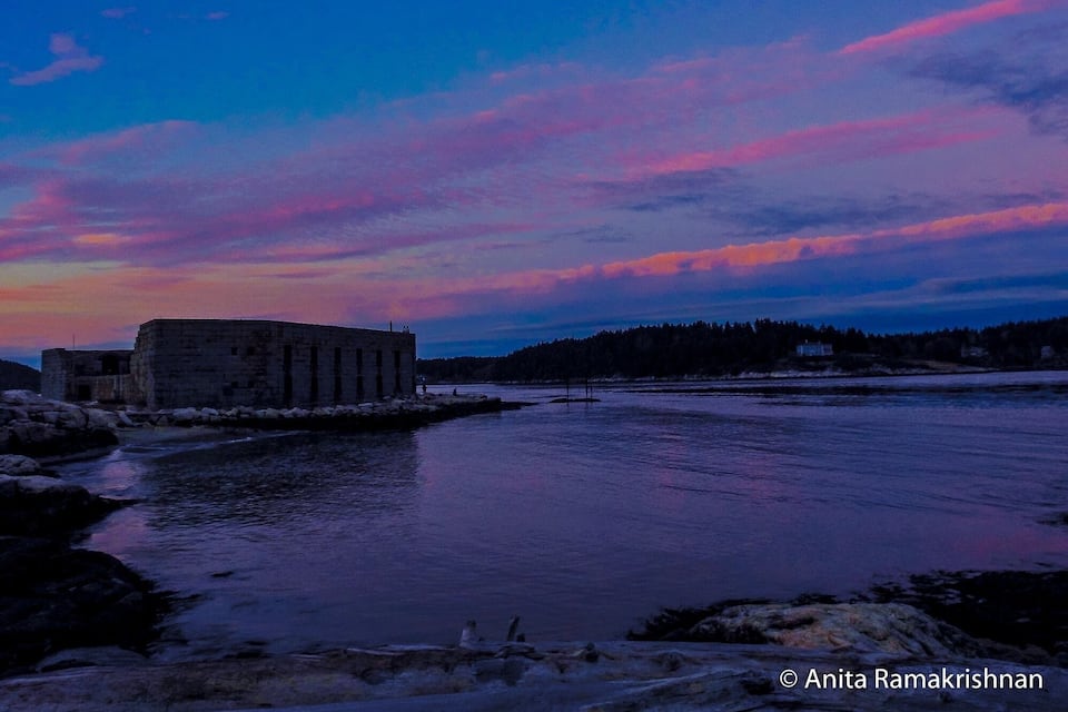 A stone building by a river at sunset.