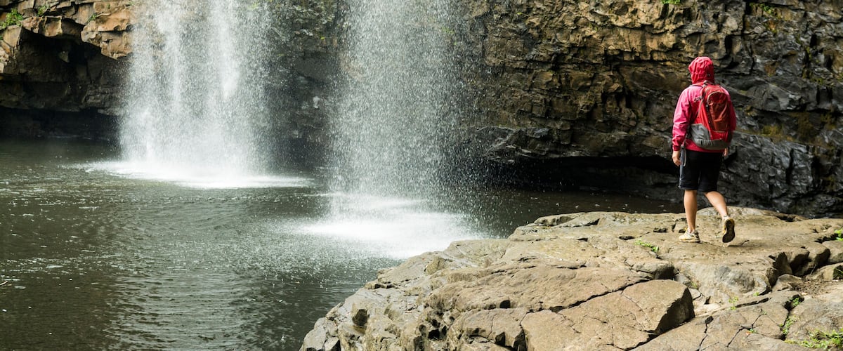 A person standing on rocks near a waterfall.