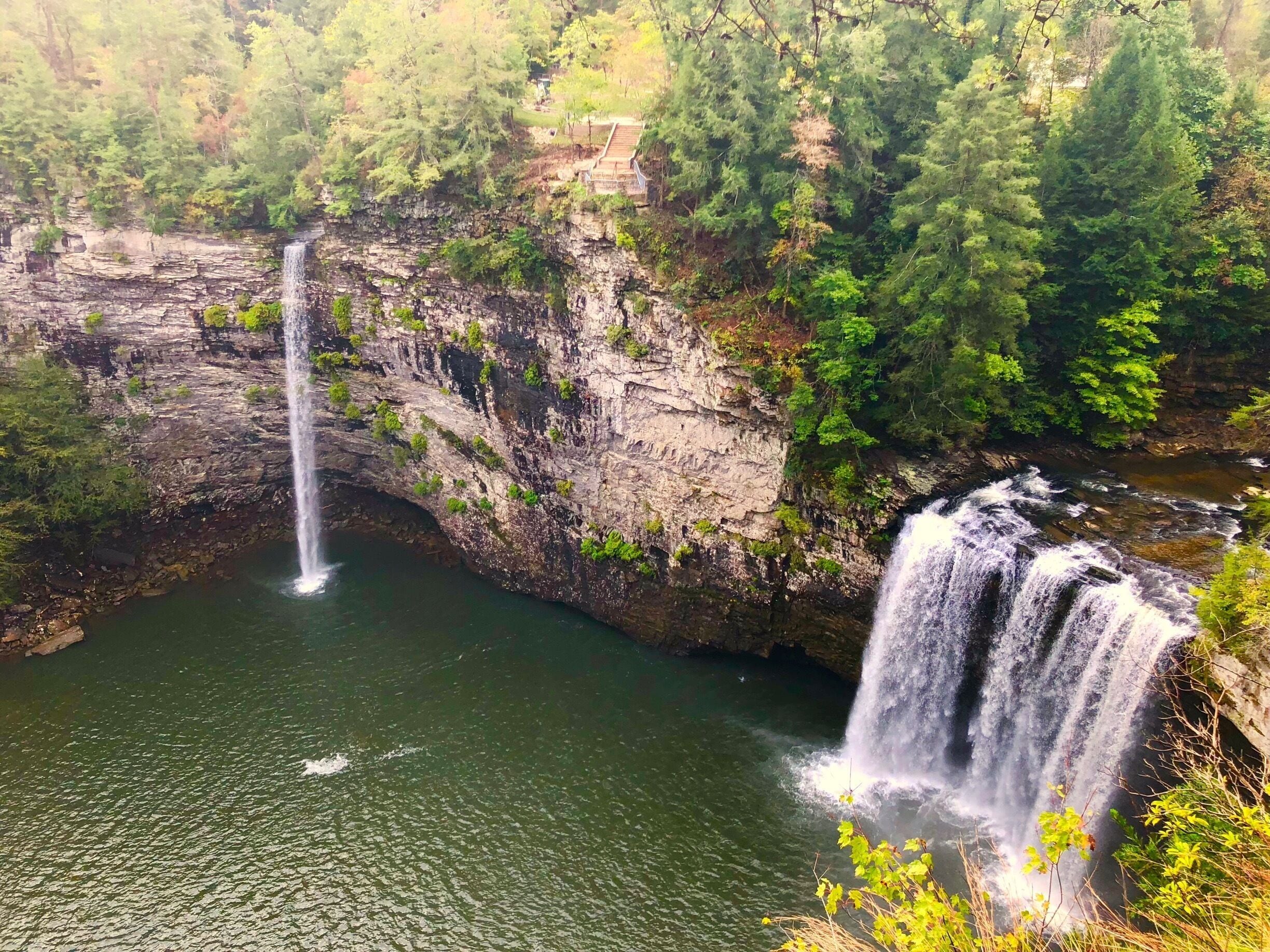 A waterfall cascading down a rocky cliff into a calm river surrounded by dense forest.