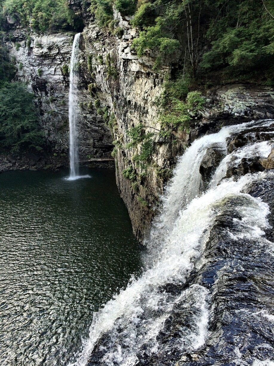 A waterfall cascading down a rocky cliff into a calm river surrounded by lush greenery.