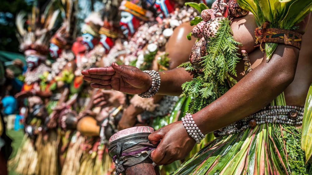 A person wearing a green skirt with red and green leaves, a beaded necklace, and a woven belt.