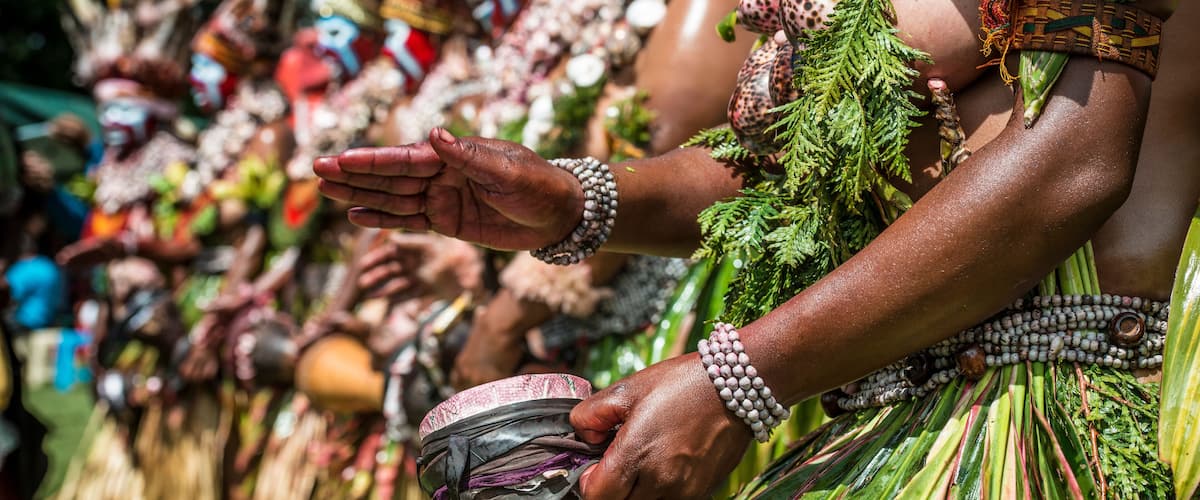 A person wearing a green skirt with red and green leaves, a beaded necklace, and a woven belt.