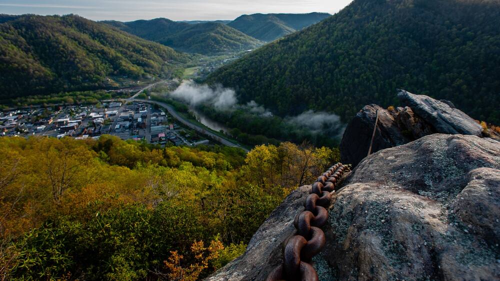 Un paysage montagneux avec une ville située dans la vallée, une route sinueuse et une chaîne d’anneaux métalliques rouillés fixés à un rocher.