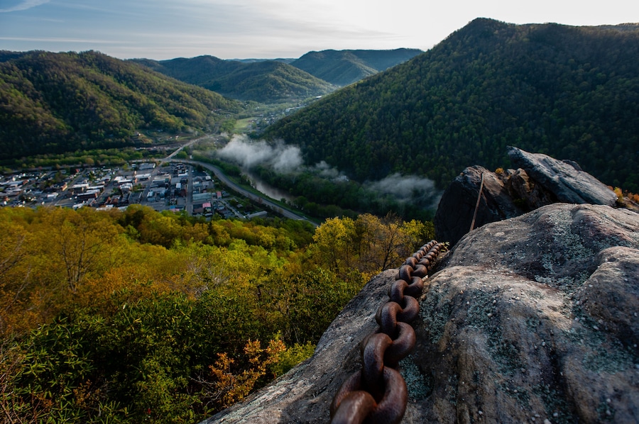 A mountainous landscape with a town in the valley, a winding road, and a chain of rusty metal rings on a rock.