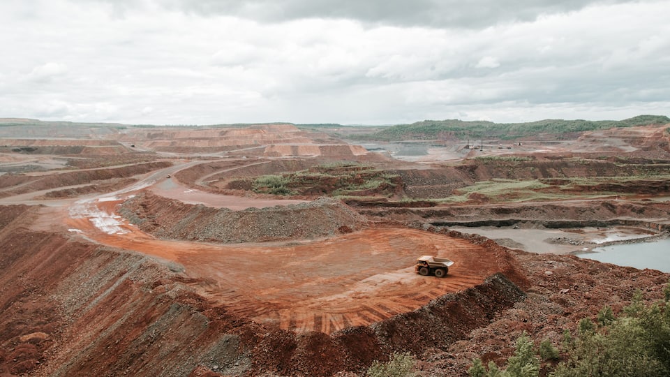 A large open-pit mine with terraced excavation areas and a truck on the right.