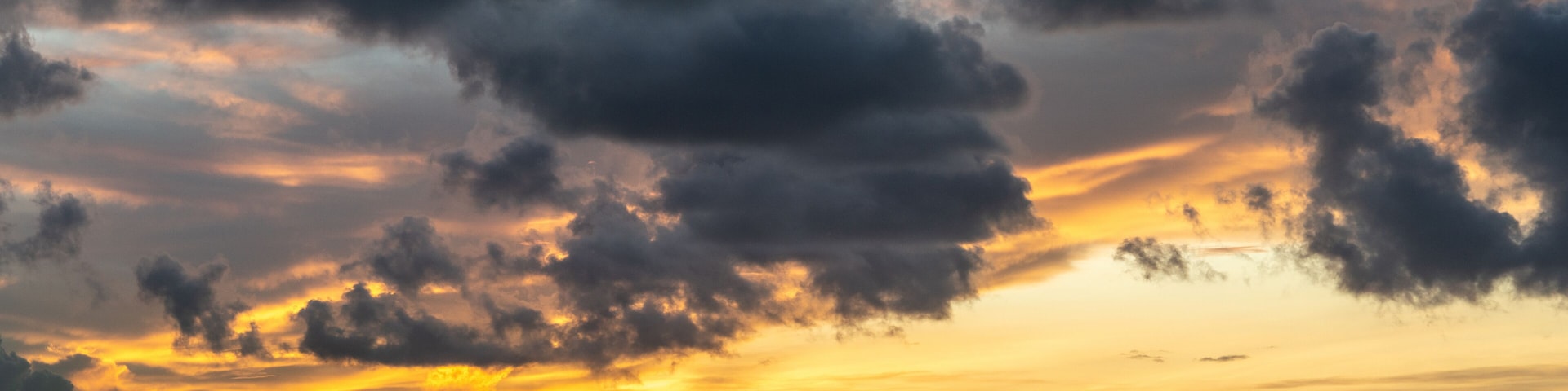 Thursday Island, Australia - February 20, 2019: Pre-sunrise shot over Torres Strait Islands Archipelago shows dark blue clouds in yellow and red light hanging over black island hills in very dark blue
