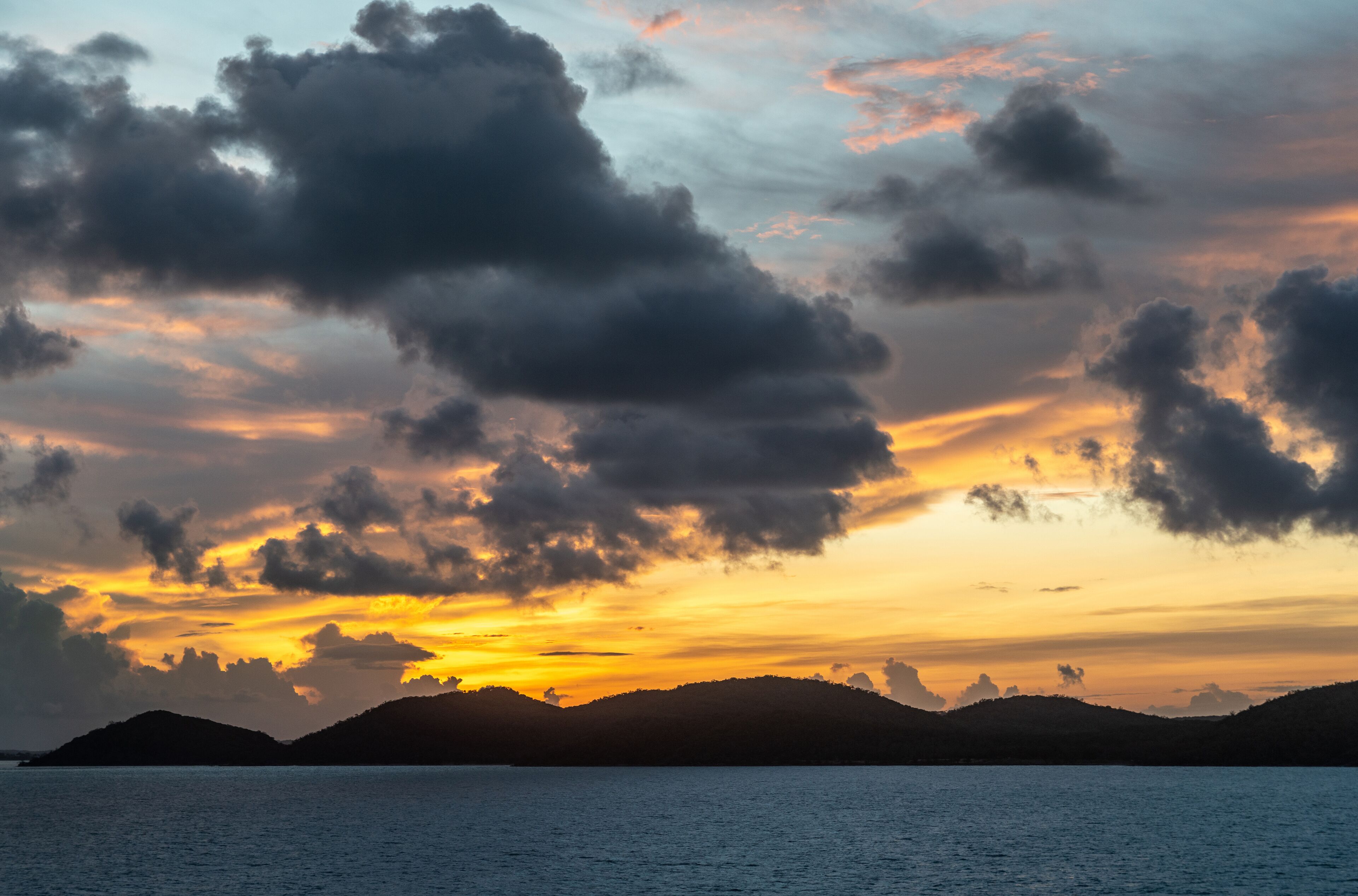 A sunset over a body of water with silhouetted hills in the background.