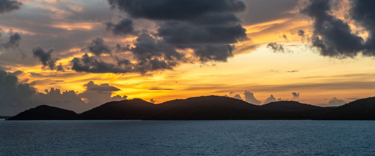 A sunset over a body of water with silhouetted hills in the background.