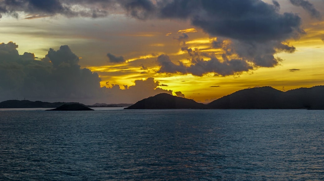 Thursday Island, Australia - February 20, 2019: Panorama of sunrise shot over Torres Strait Islands Archipelago shows dark blue clouds in yellow and red light hanging over black island hills in very d