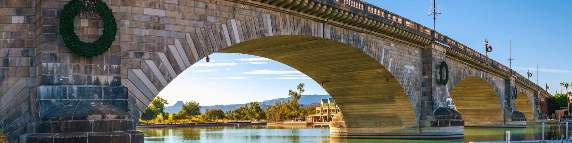 A stone bridge with arches over a calm river, decorated with wreaths and a Christmas tree.
