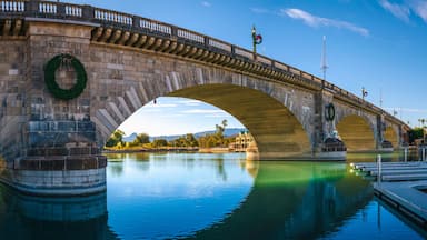 Uma ponte de pedra com arcos sobre um rio calmo, adornada com guirlandas e um pinheiro de Natal.