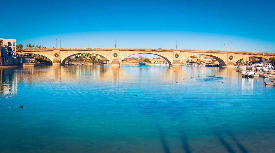 Uma ponte de pedra sobre um rio calmo, com barcos e céu azul límpido.