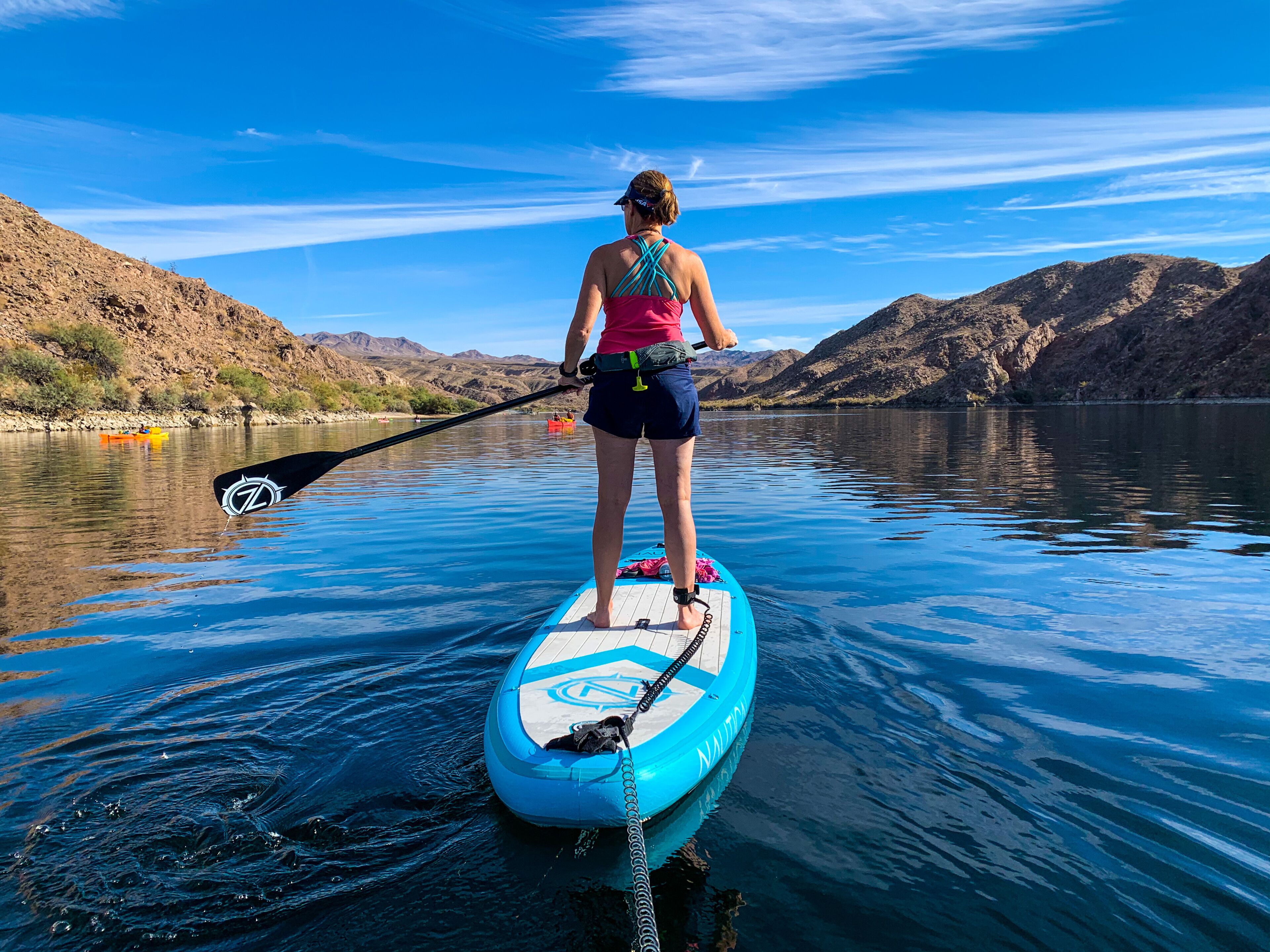 Uma pessoa praticando paddleboard em um lago calmo, com montanhas ao fundo.