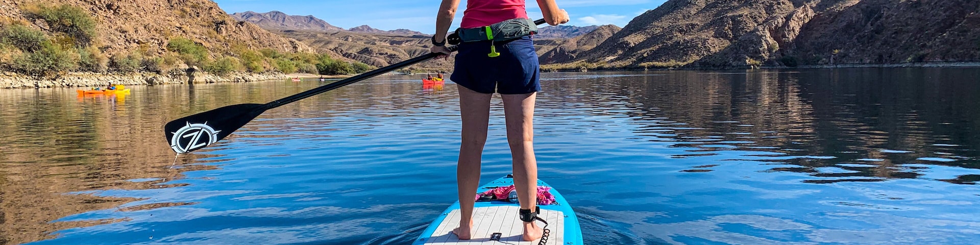Uma pessoa praticando paddleboard em um lago calmo, com montanhas ao fundo.