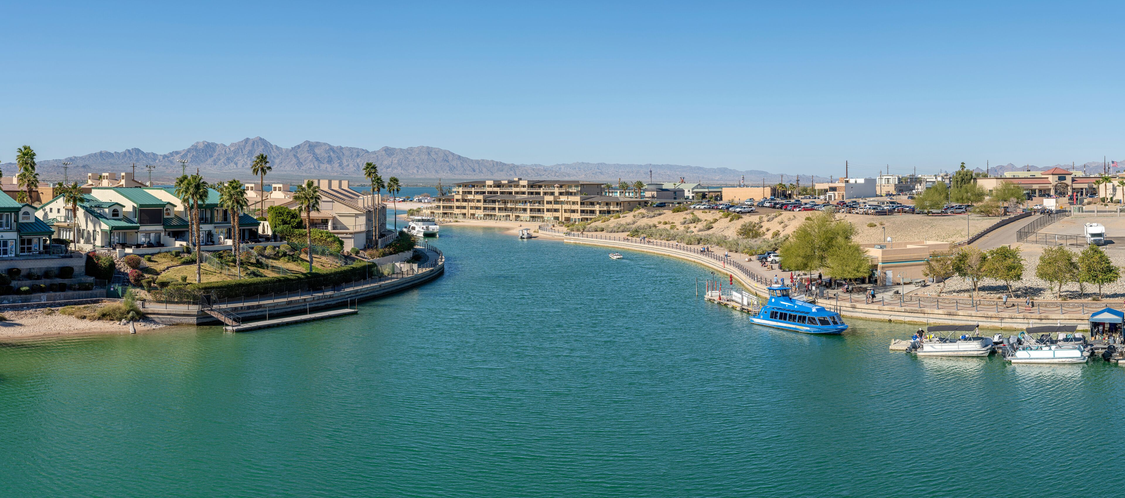 A coastal town with a marina, boats, and a mountainous backdrop.