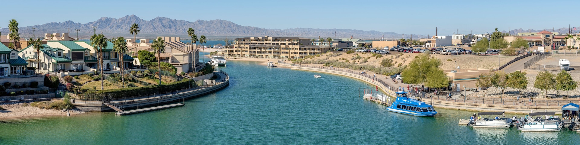 A coastal town with a marina, boats, and a mountainous backdrop.