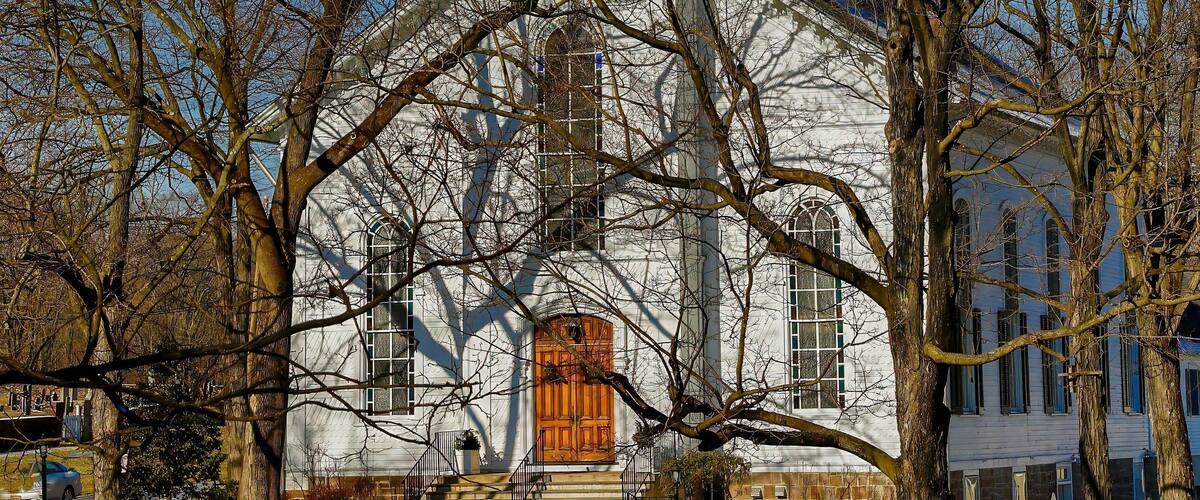 A white church with a green roof and a wooden door, surrounded by leafless trees.