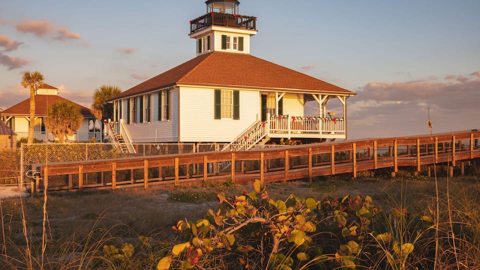 A white building with a red roof, a wooden deck, and a lighthouse on top.