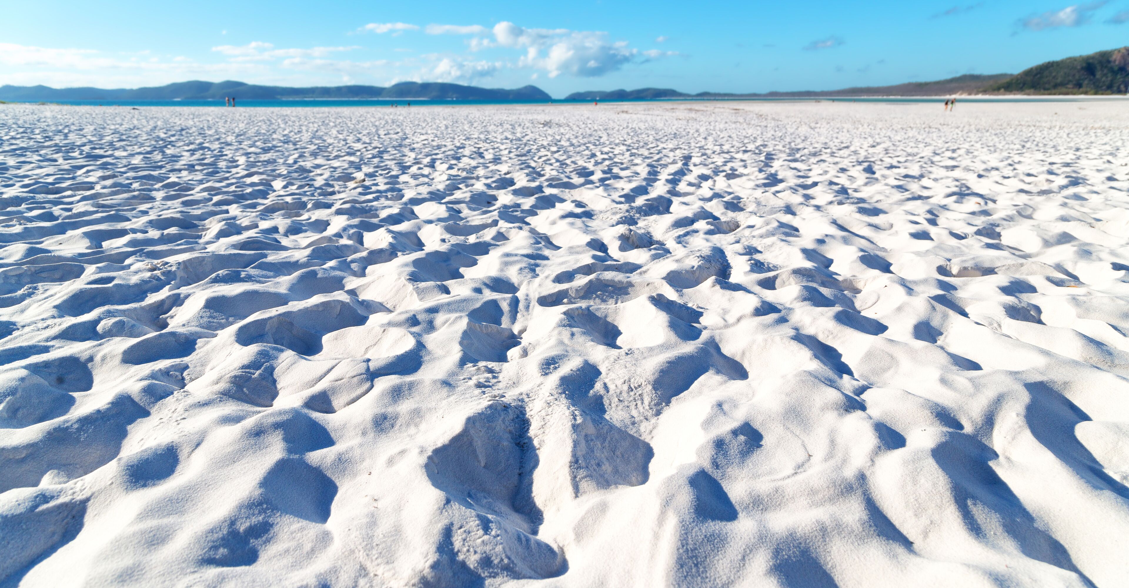 A vast, undisturbed snow-covered beach with footprints leading towards the water.