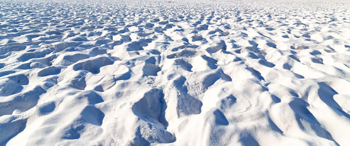 A vast, undisturbed snow-covered beach with footprints leading towards the water.