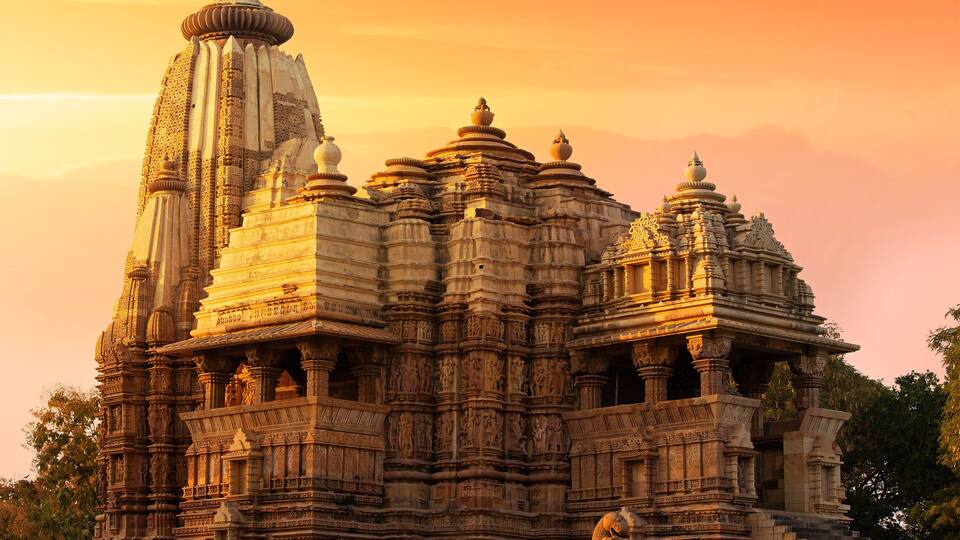 A detailed stone temple with intricate carvings and multiple spires, set against a sunset sky.