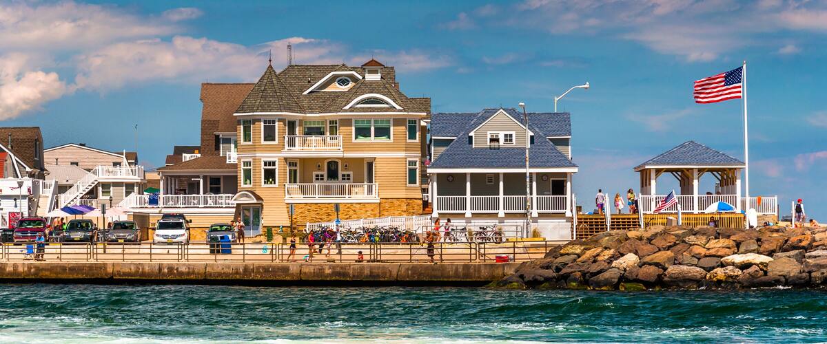 A coastal town with a prominent yellow house, a gazebo with an American flag, and a rocky breakwater.
