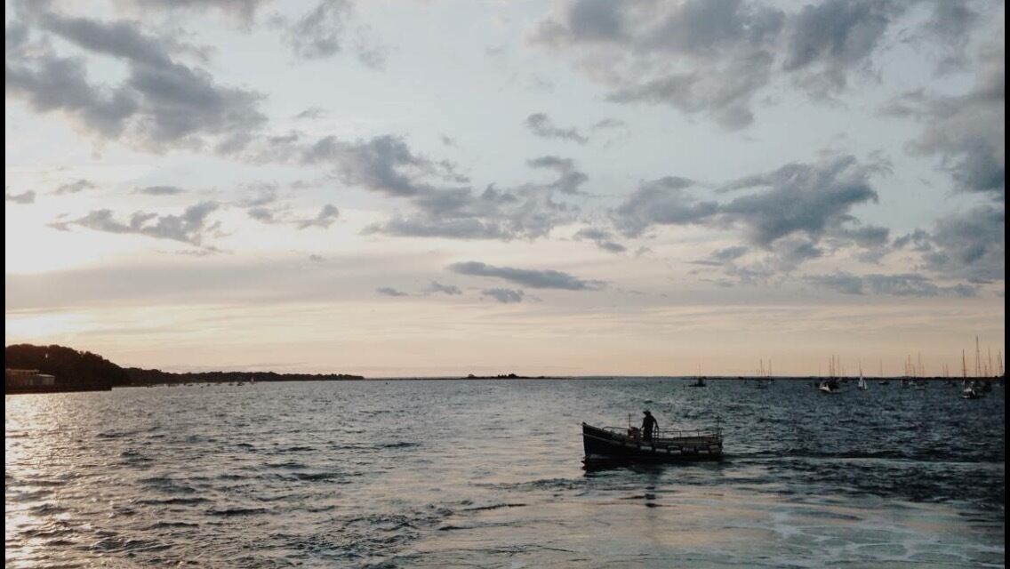A calm sea with a boat in the foreground and sailboats in the distance.