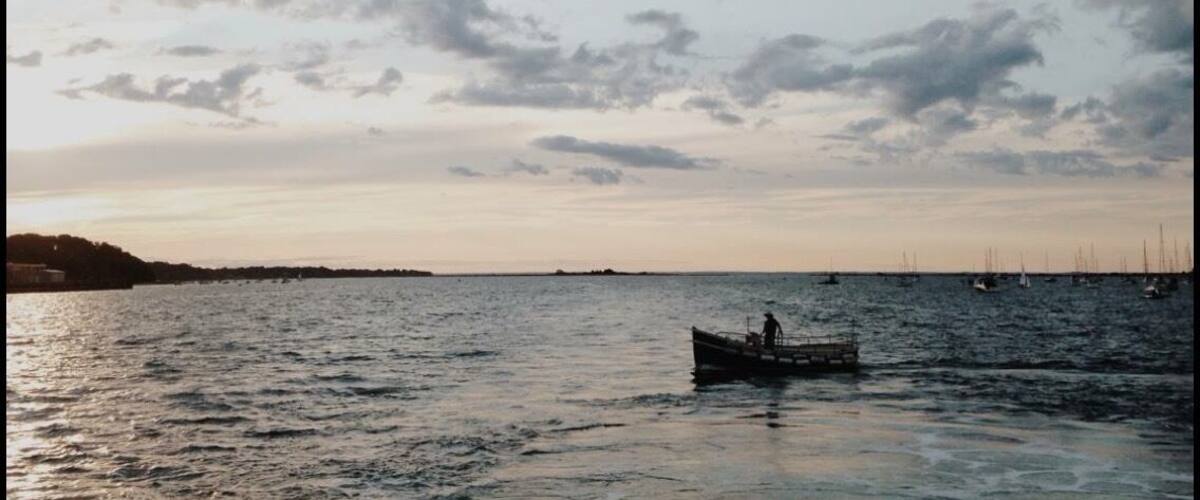 A calm sea with a boat in the foreground and sailboats in the distance.