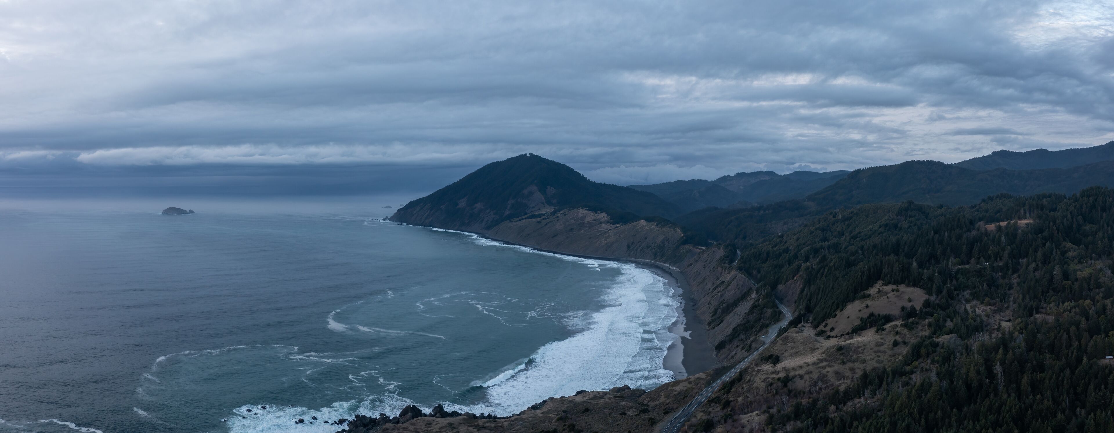 Un paisaje costero con una montaña escarpada, un camino sinuoso y una playa.