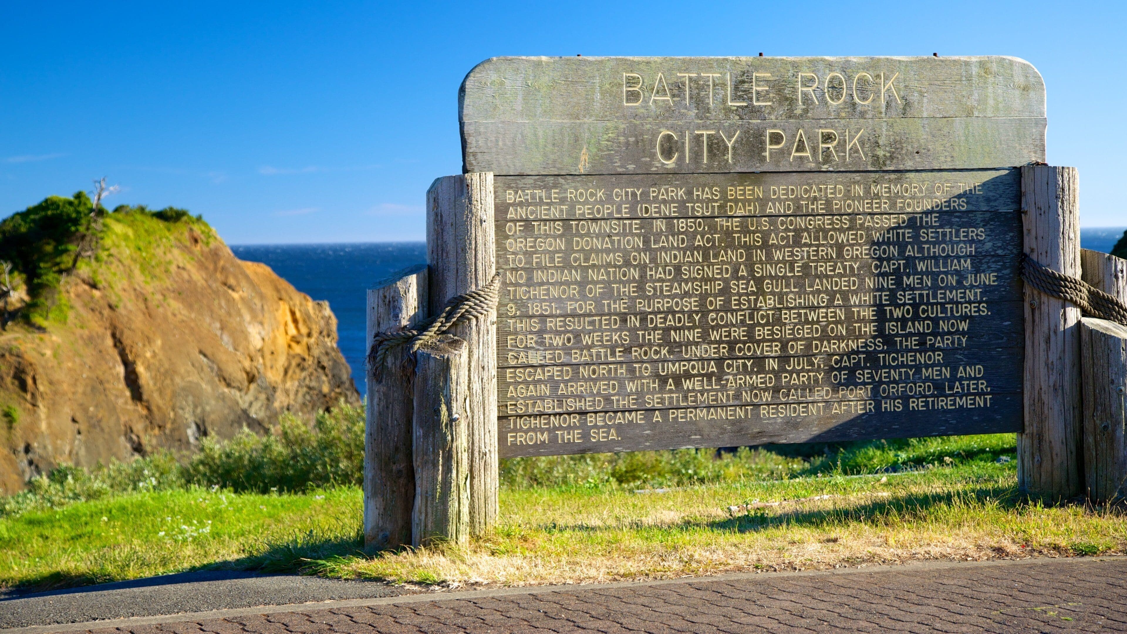 A historical marker at Battle Rock City Park with a coastal background.