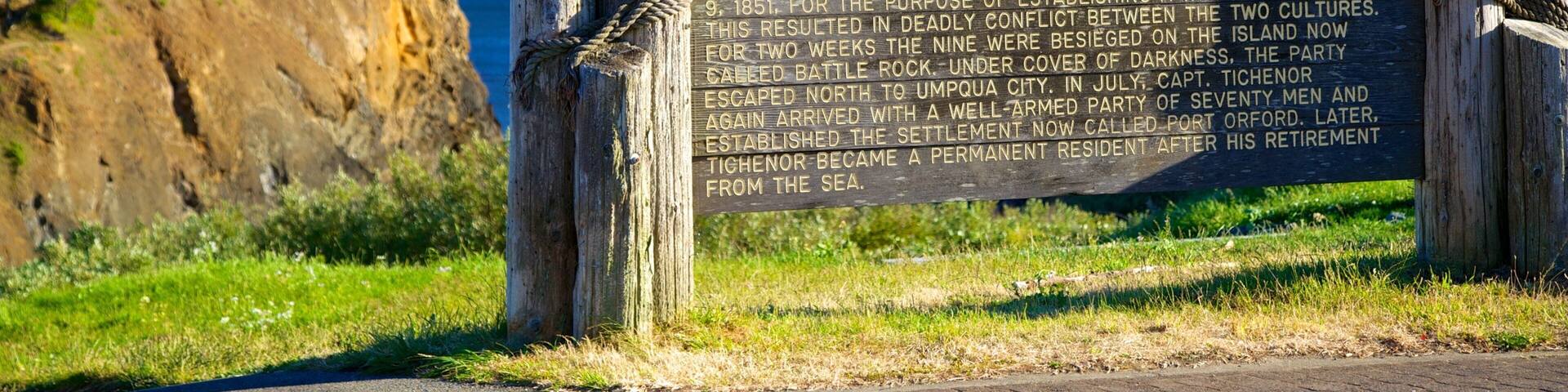 A historical marker at Battle Rock City Park with a coastal background.
